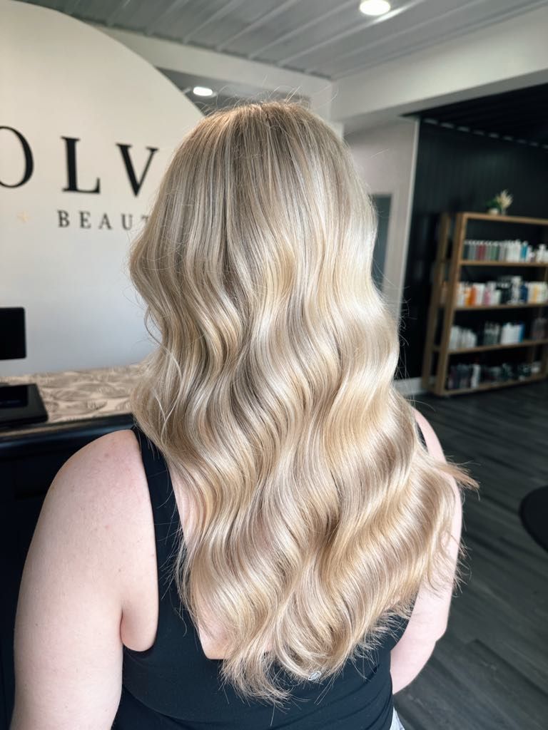 Woman with wavy, light blonde hair in a salon. She is wearing a black top, and the salon has black and white decor.