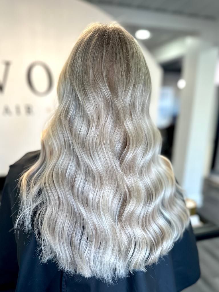 Woman with long, wavy, light blonde hair. Back view with blurred background of a hair salon.