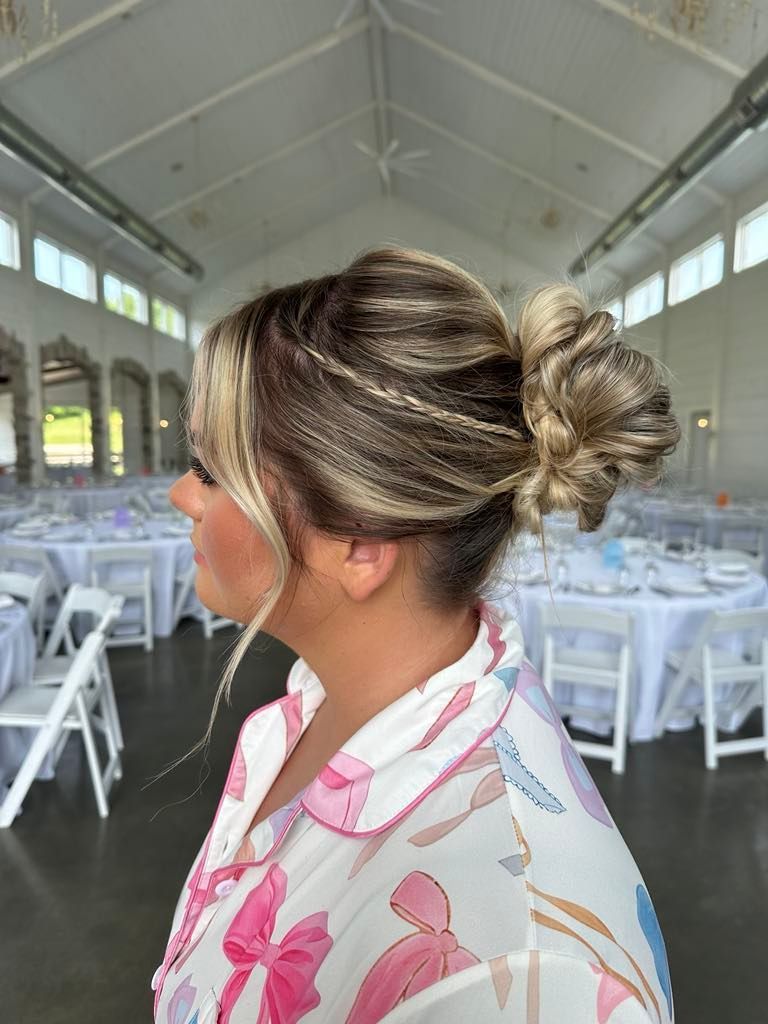 Woman with a blonde and brown updo hairstyle, wearing a floral shirt, stands indoors with tables set for an event.
