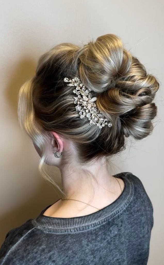 Woman with blonde updo hairstyle, adorned with a silver hair clip, wearing a grey sweater, turned with her back to the viewer.