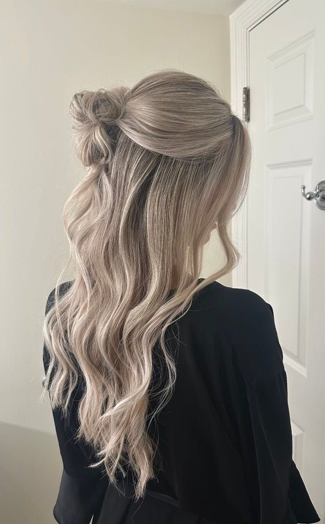 Woman with long, light-colored hair styled half-up with crimped sections and loose waves. She wears a dark shirt indoors, near a white door.