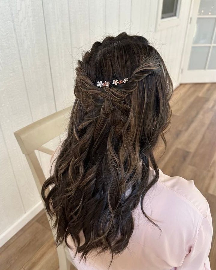 Woman with dark hair styled in a half-up braid with loose waves, wearing a flower hair clip.