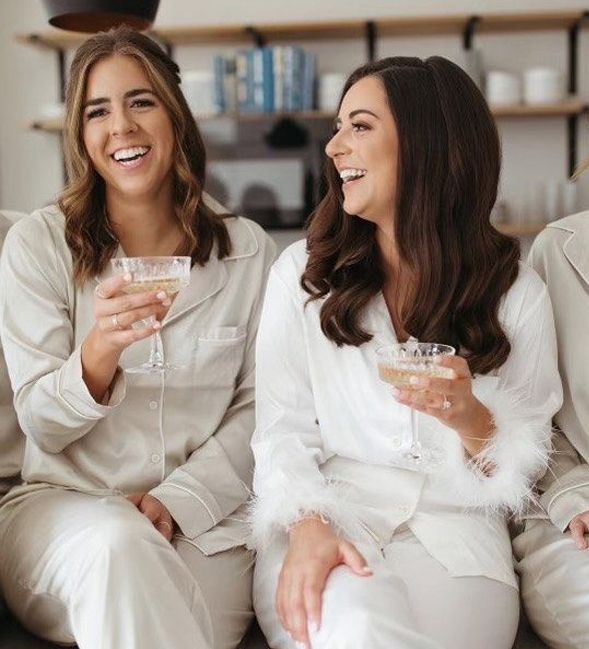 Two women in matching pajamas laughing while holding champagne glasses, indoors.