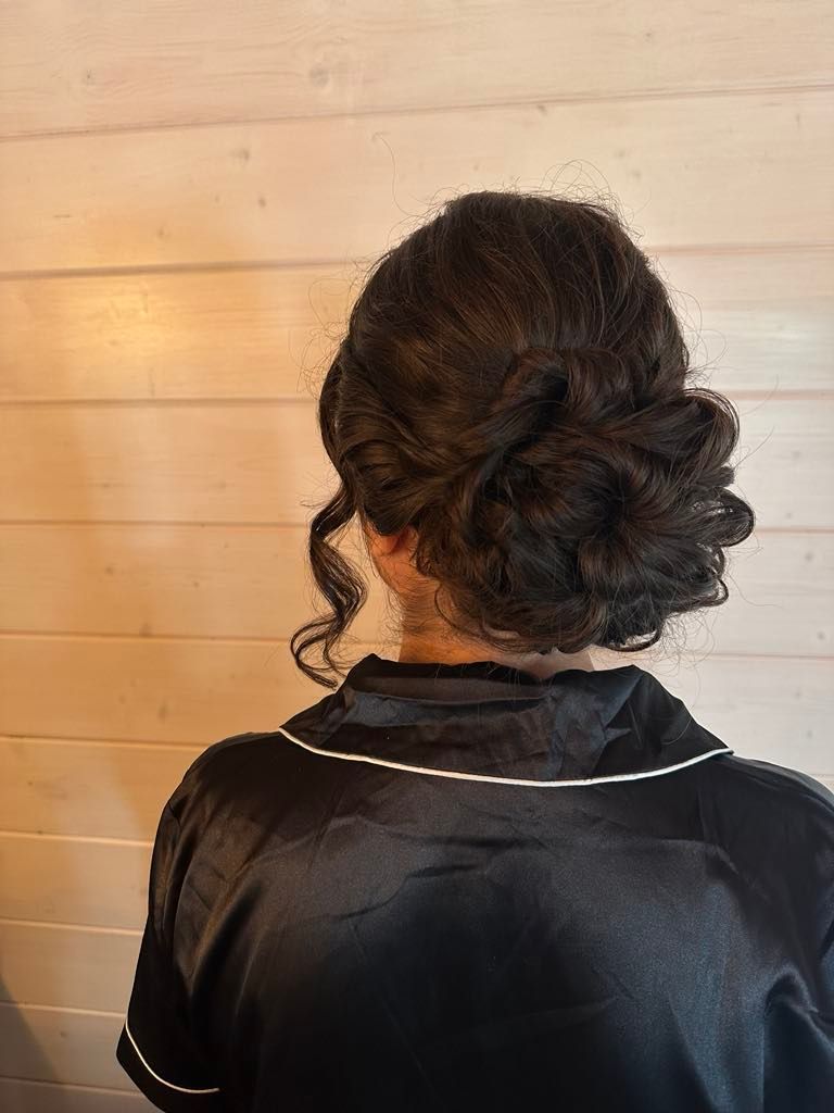 A woman with dark hair styled in an updo wearing a black satin robe against a light wooden background.