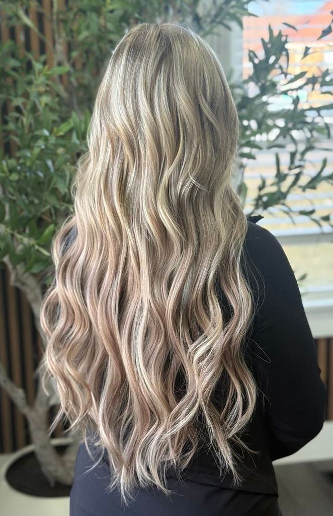 Back view of long wavy blonde hair with dark roots, falling over a black top indoors
