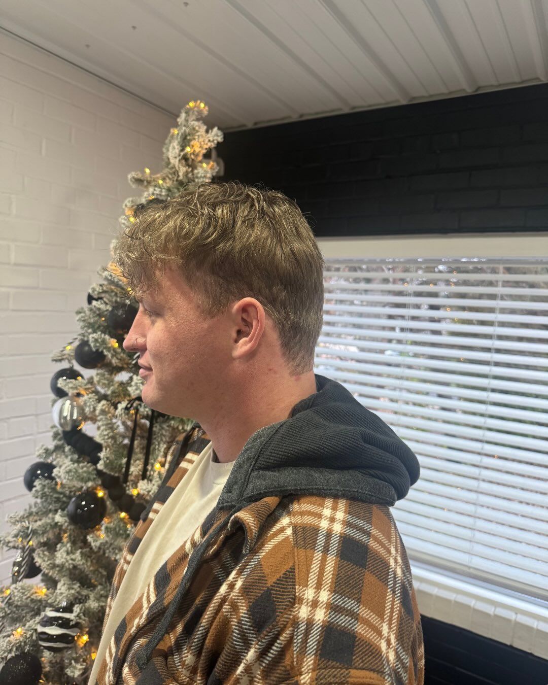 Person in brown plaid shirt, grey hooded sweatshirt, Christmas tree in background.