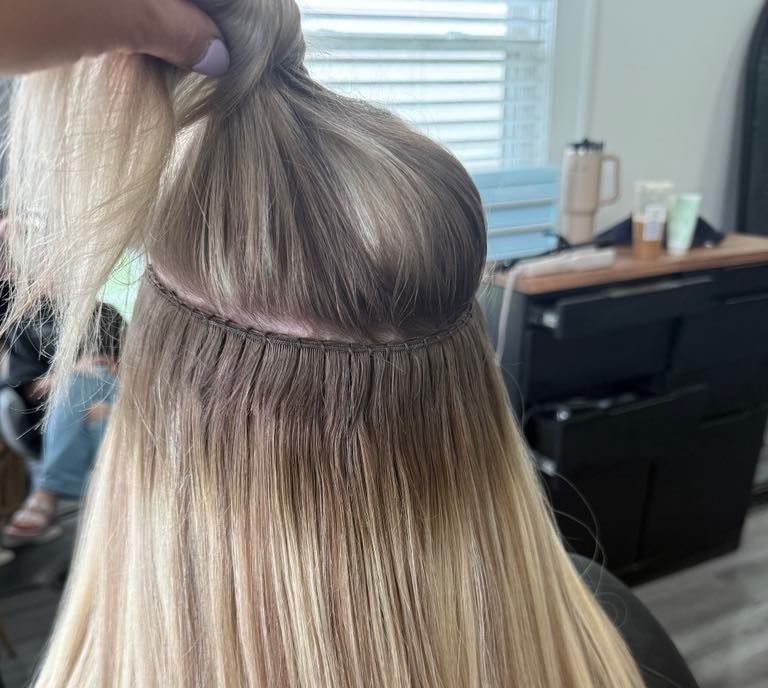 A person lifting a section of blonde hair to reveal a beaded row hair extension installation.