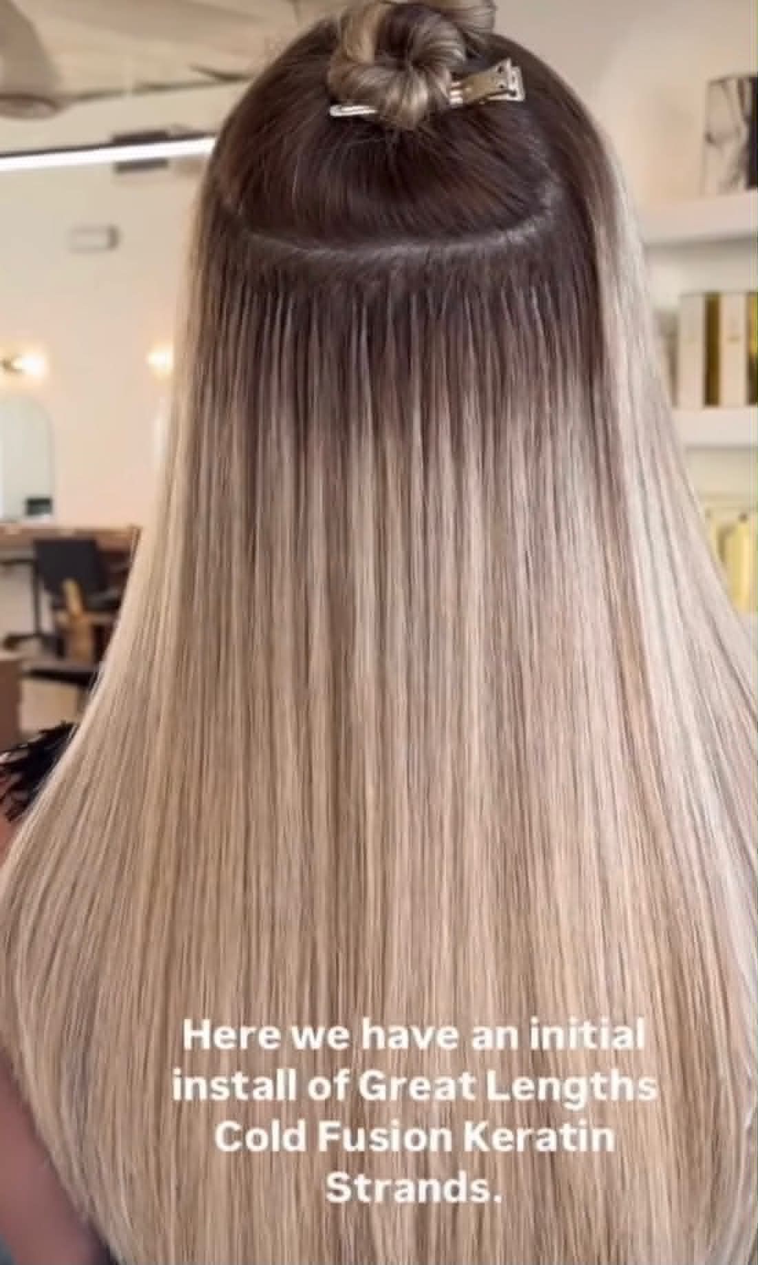 A person with long, wavy brown hair seen from behind, standing in front of a salon sign labeled