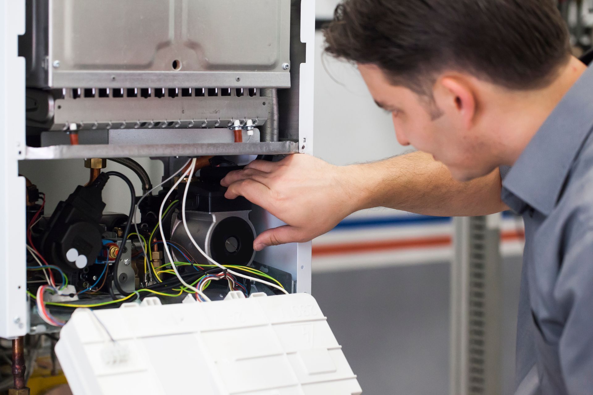Man working on the interior of a heating system, inspecting wires and parts.
