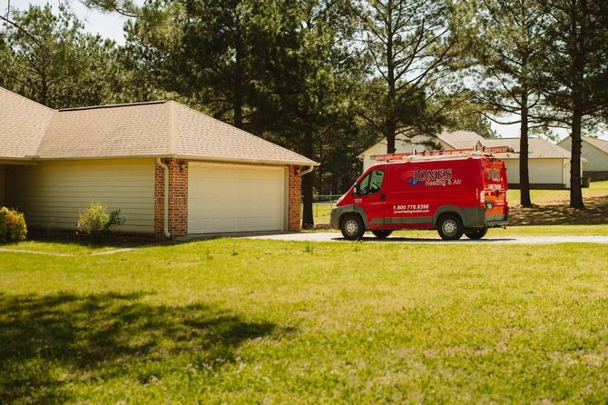 Red service van parked in front of a house, possibly for HVAC repair or maintenance on a sunny day.