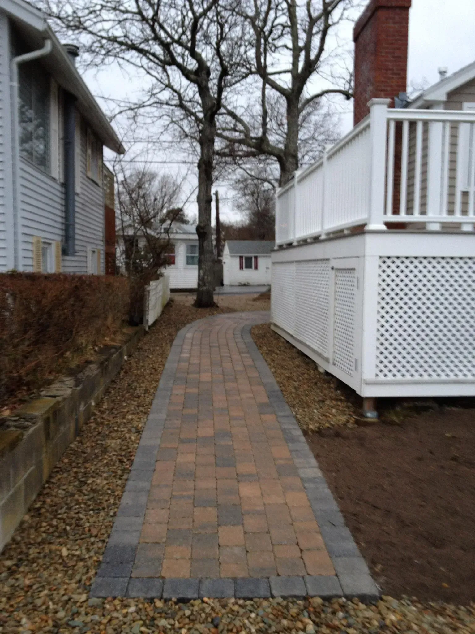 A brick walkway leading to a house with a white deck
