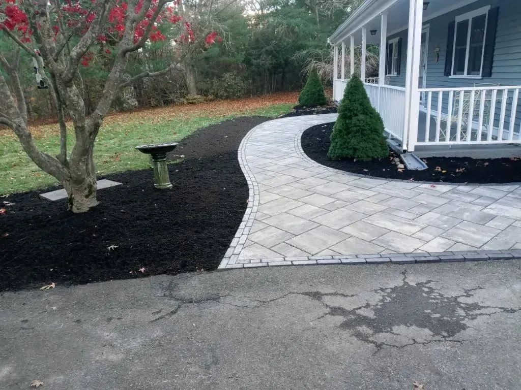 A brick walkway leading to a house with a porch.