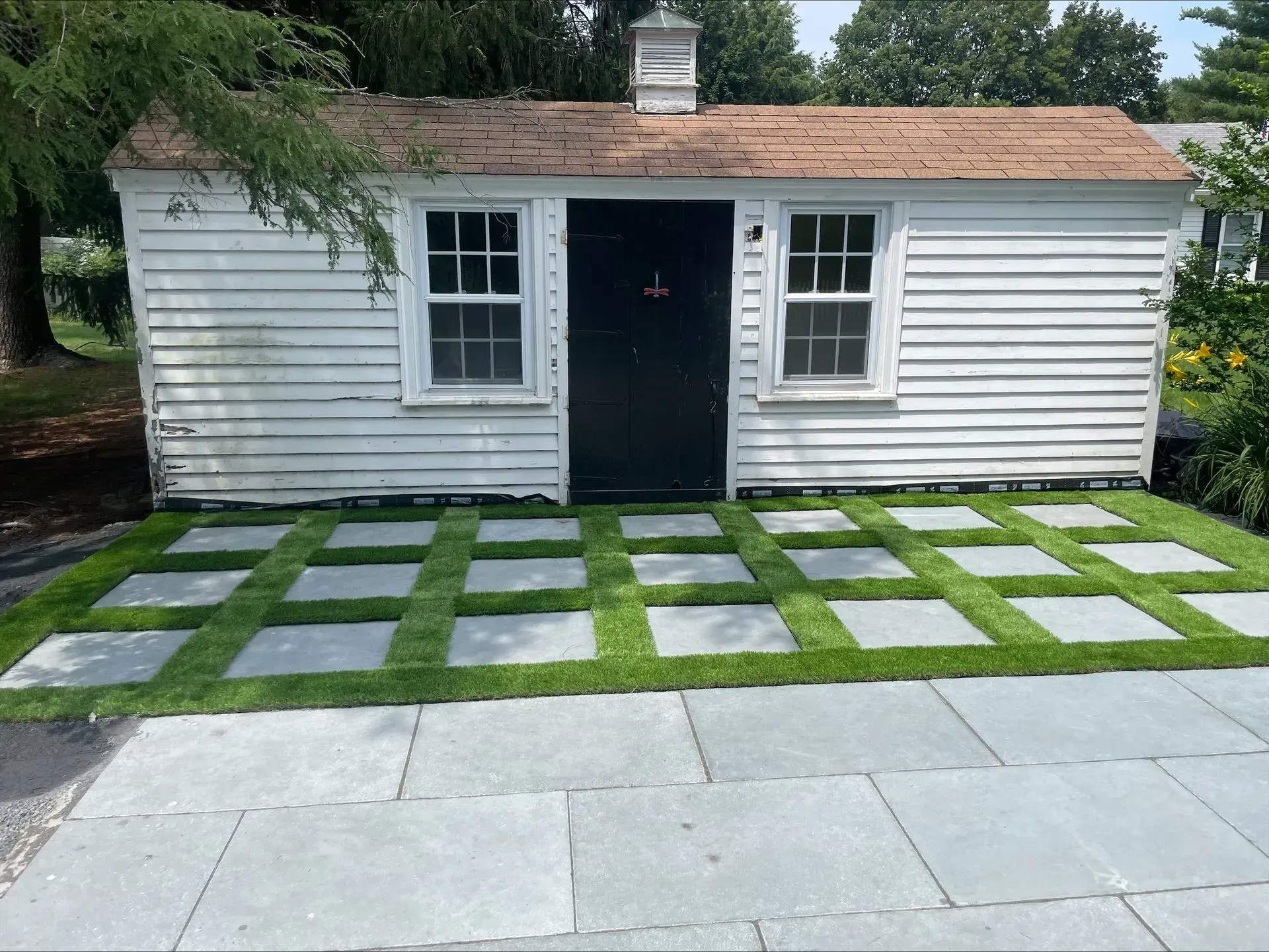 A white shed with a black door and a lawn in front of it