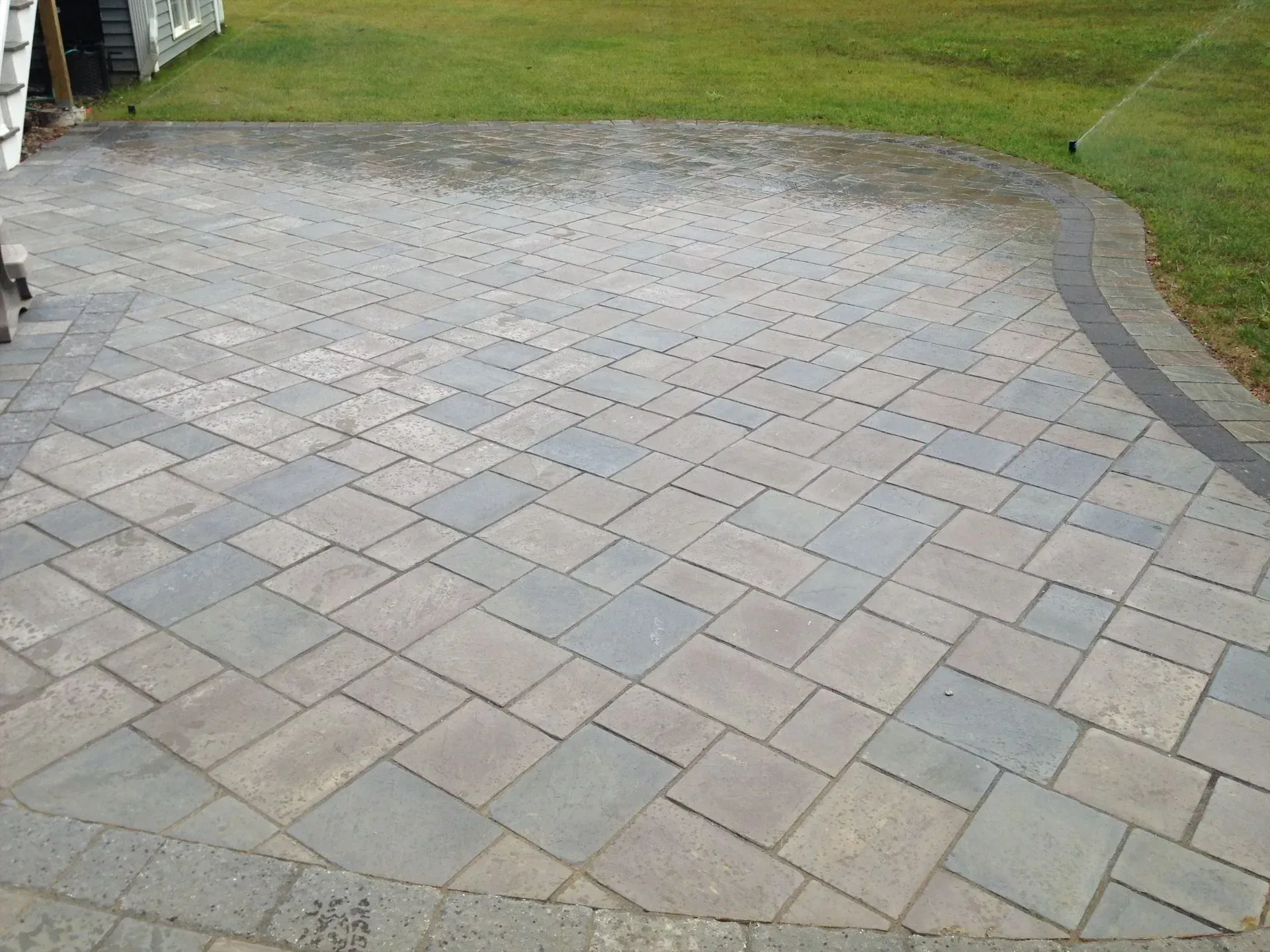 A brick patio with a sprinkler in the background