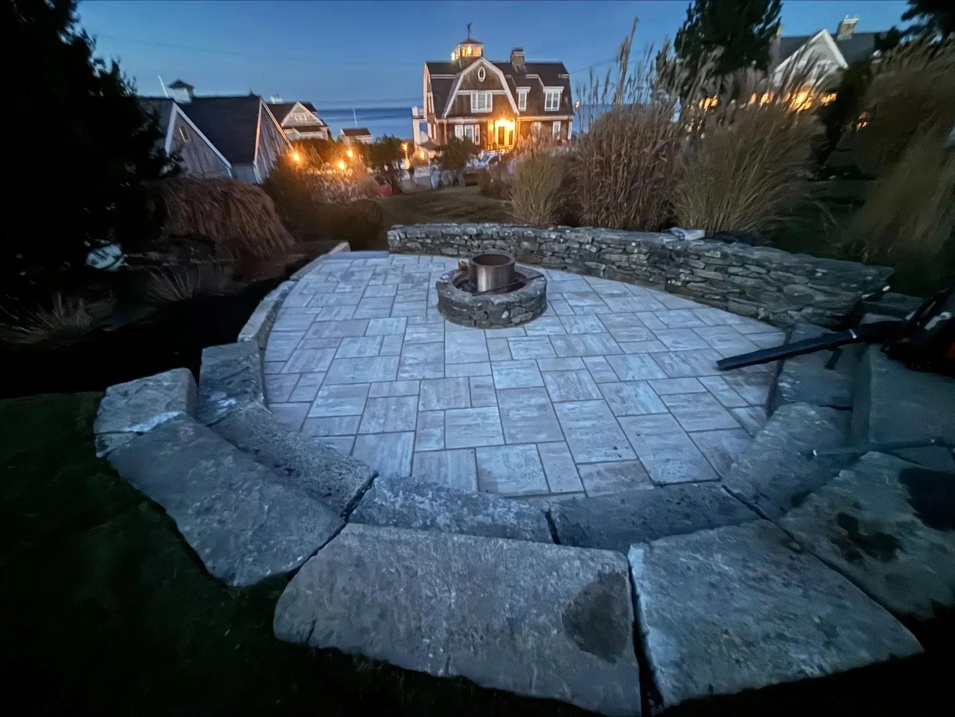 A fire pit in the middle of a patio with a house in the background.
