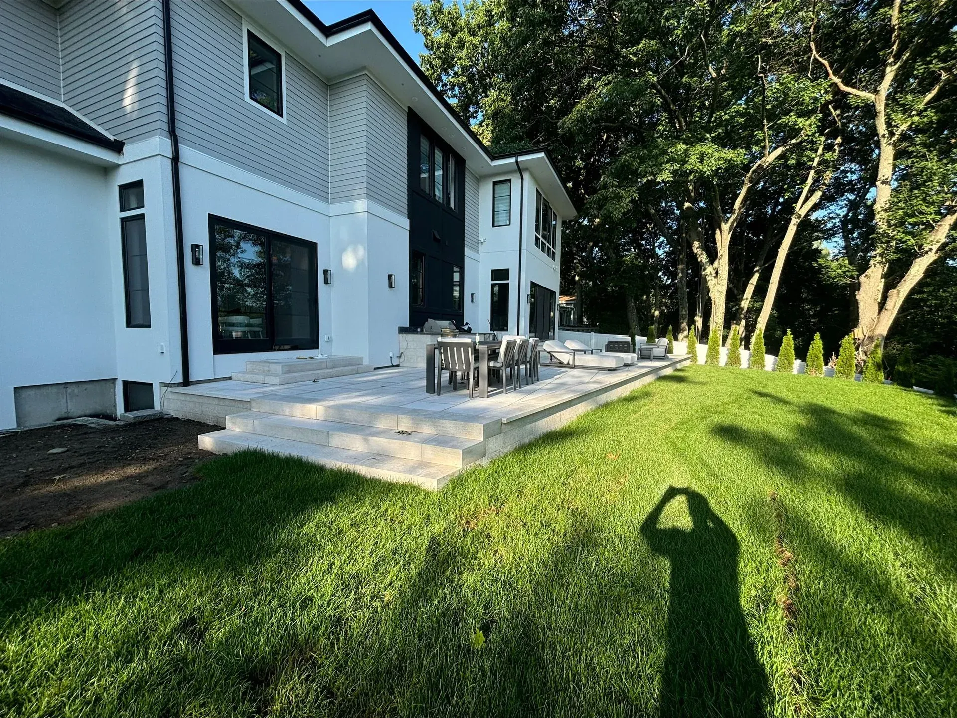 A shadow of a person is cast on the grass in front of a large house.