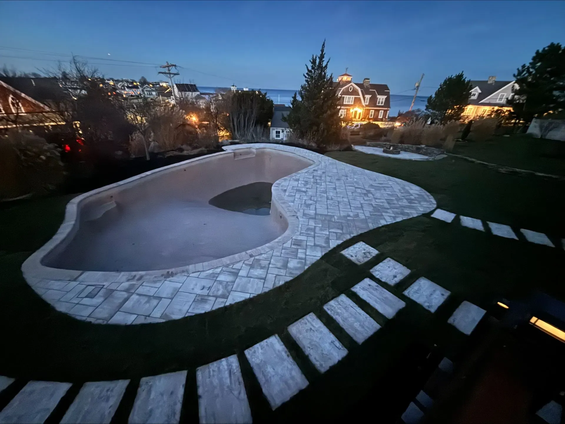 A large swimming pool is surrounded by a lush green lawn at night.