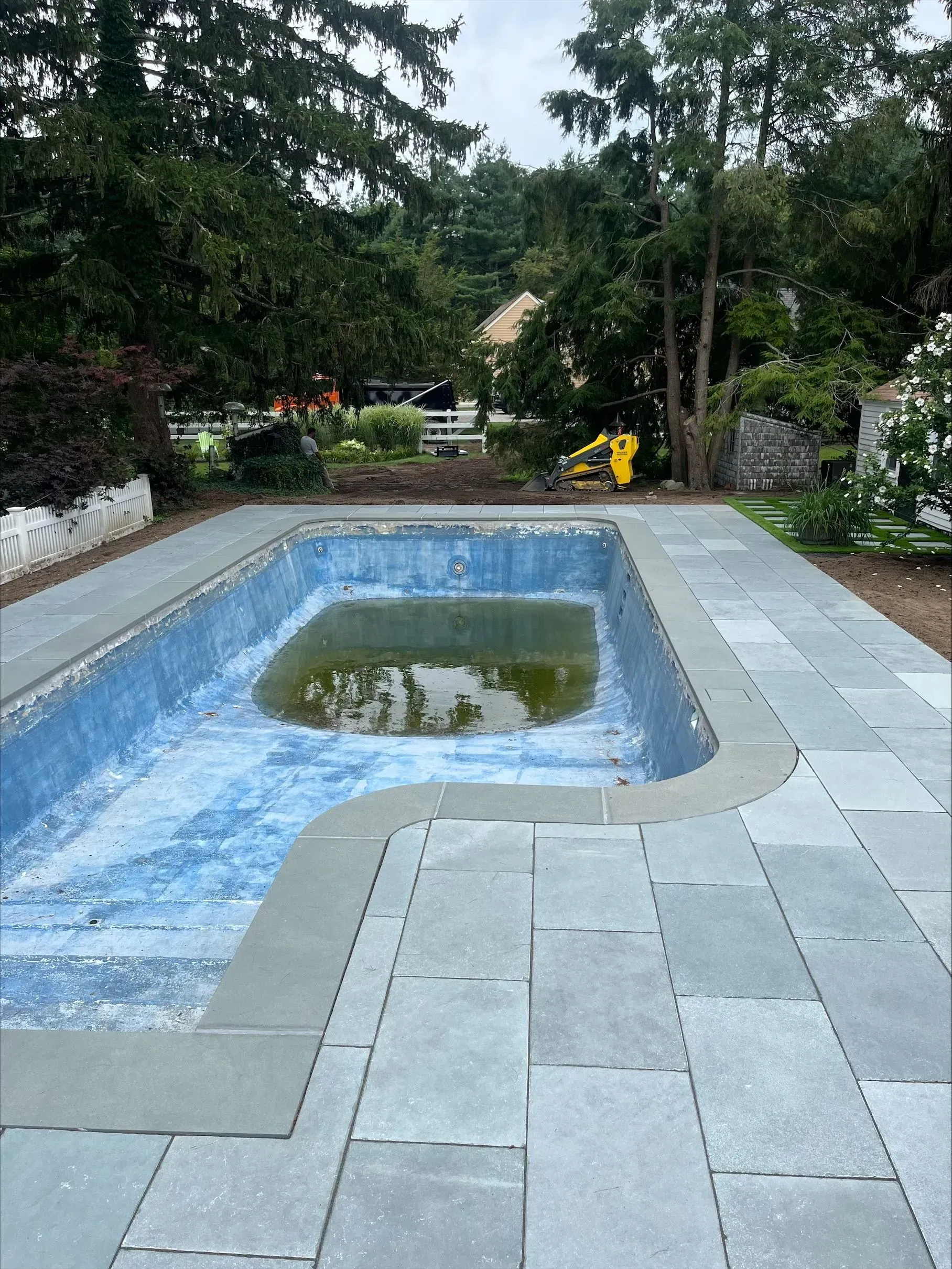 A large swimming pool is surrounded by trees and a patio.