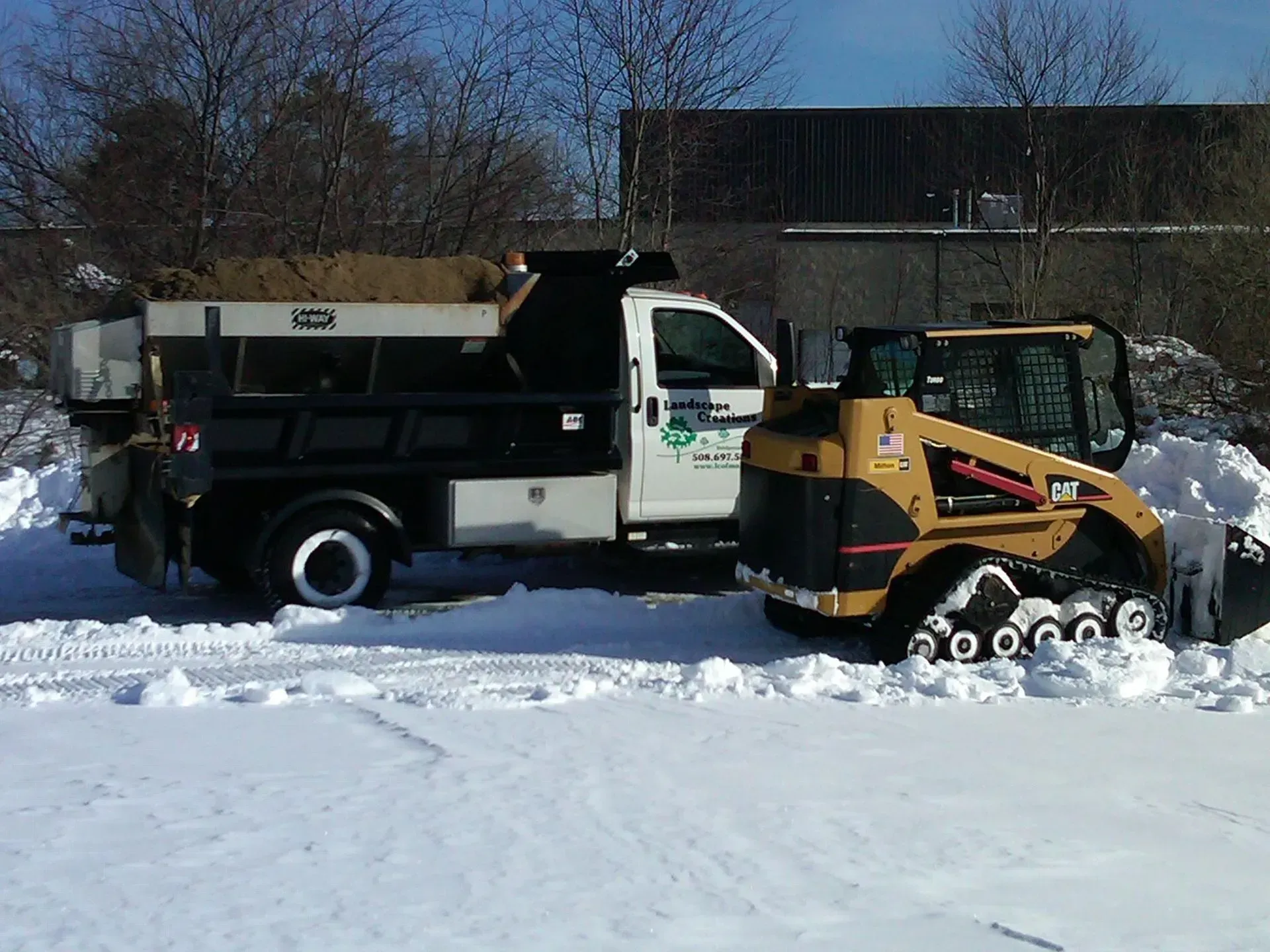 A snow plow is parked next to a dump truck in the snow