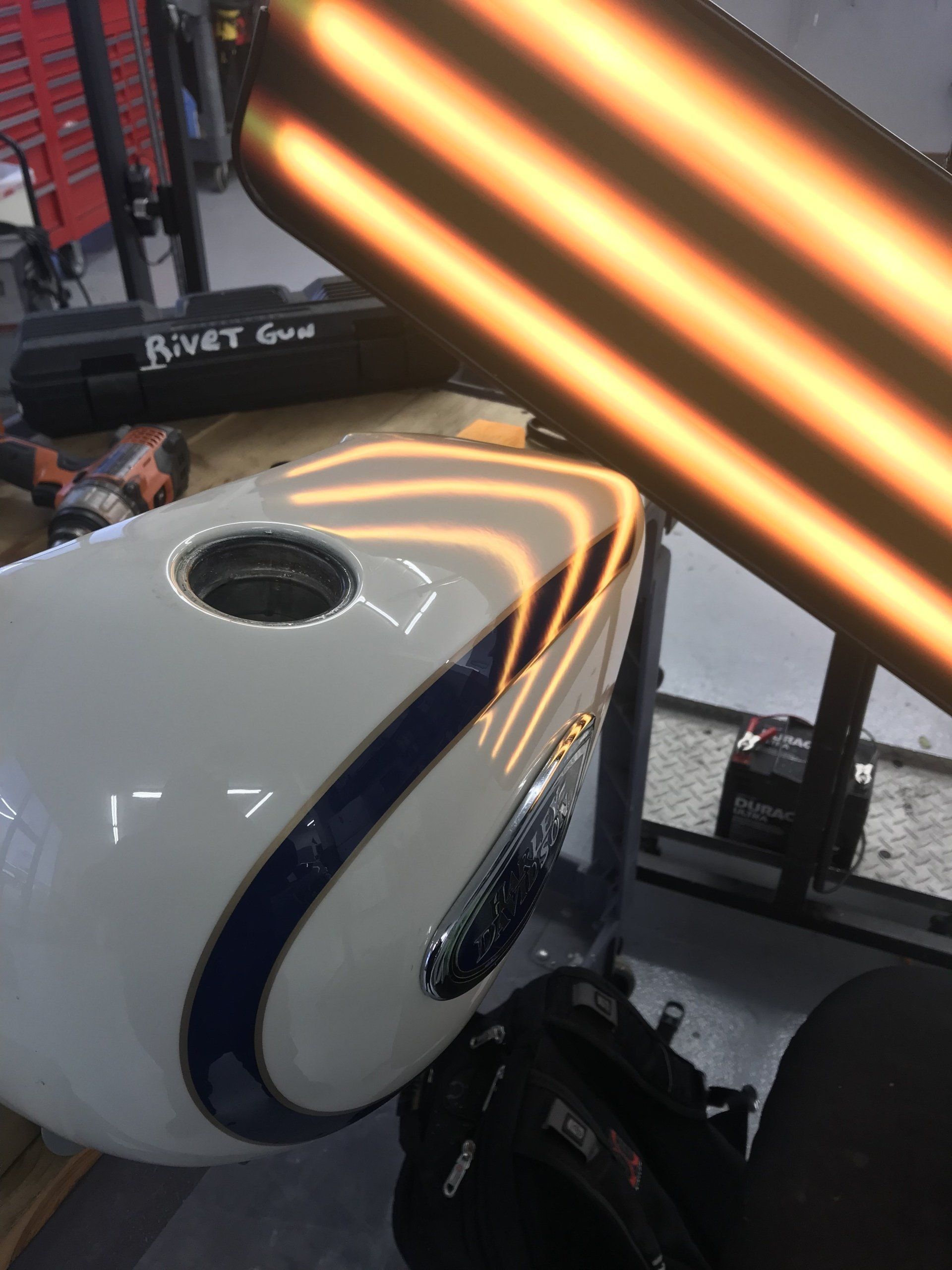 Motorcycle gas tank under specialized light for dent removal. White and blue paint.