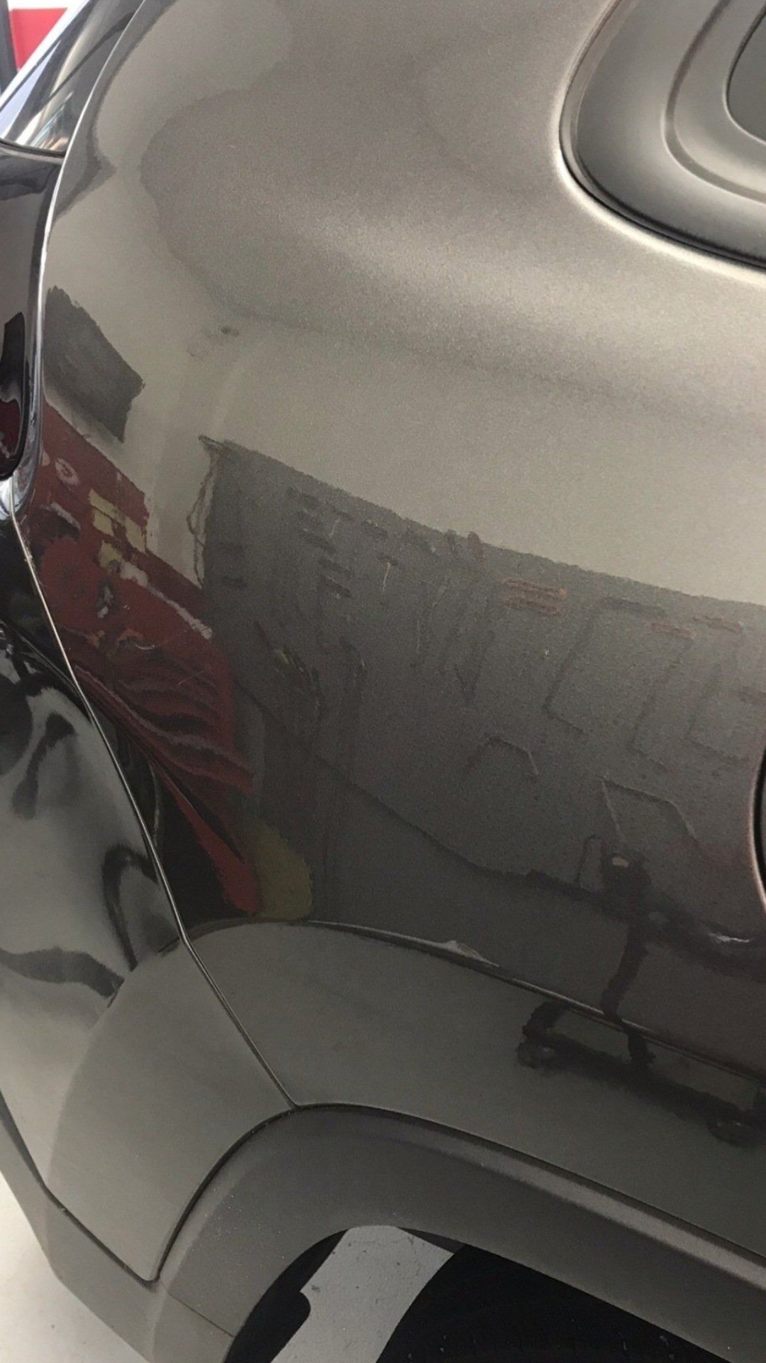 Close-up of a dark gray car's side panel, showing reflections and a black wheel arch.
