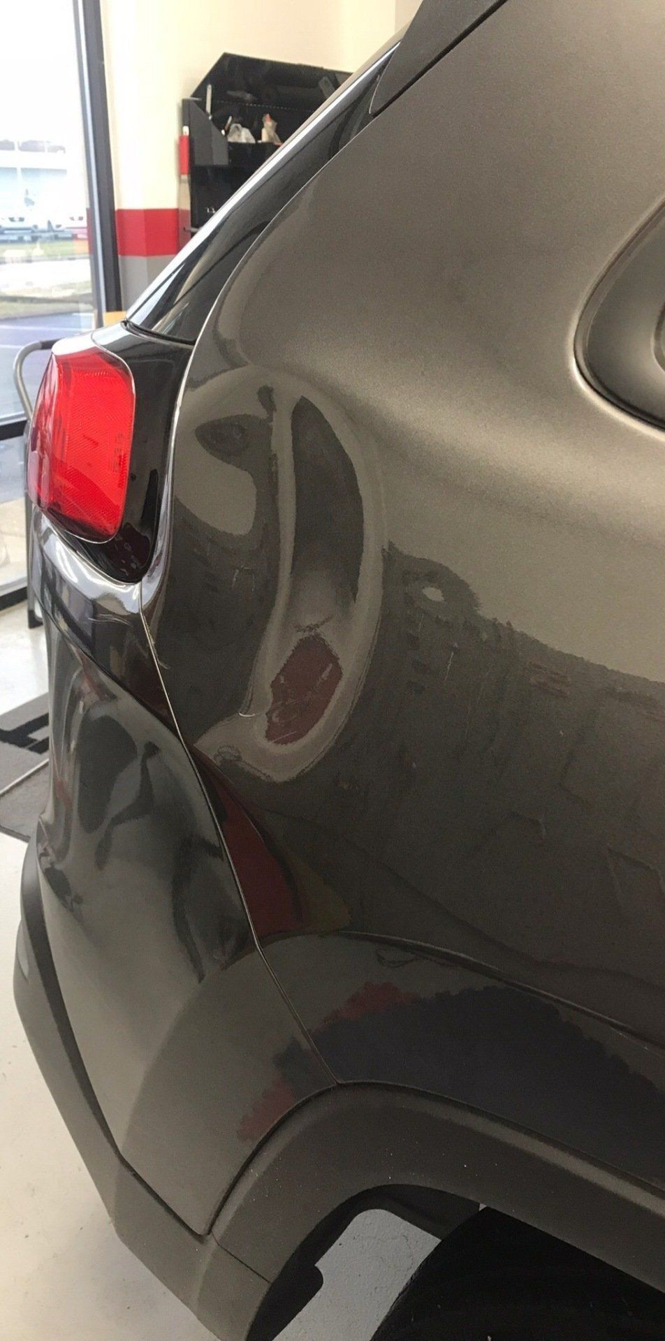 Gray car's dented rear quarter panel, showing a prominent dent on the side.