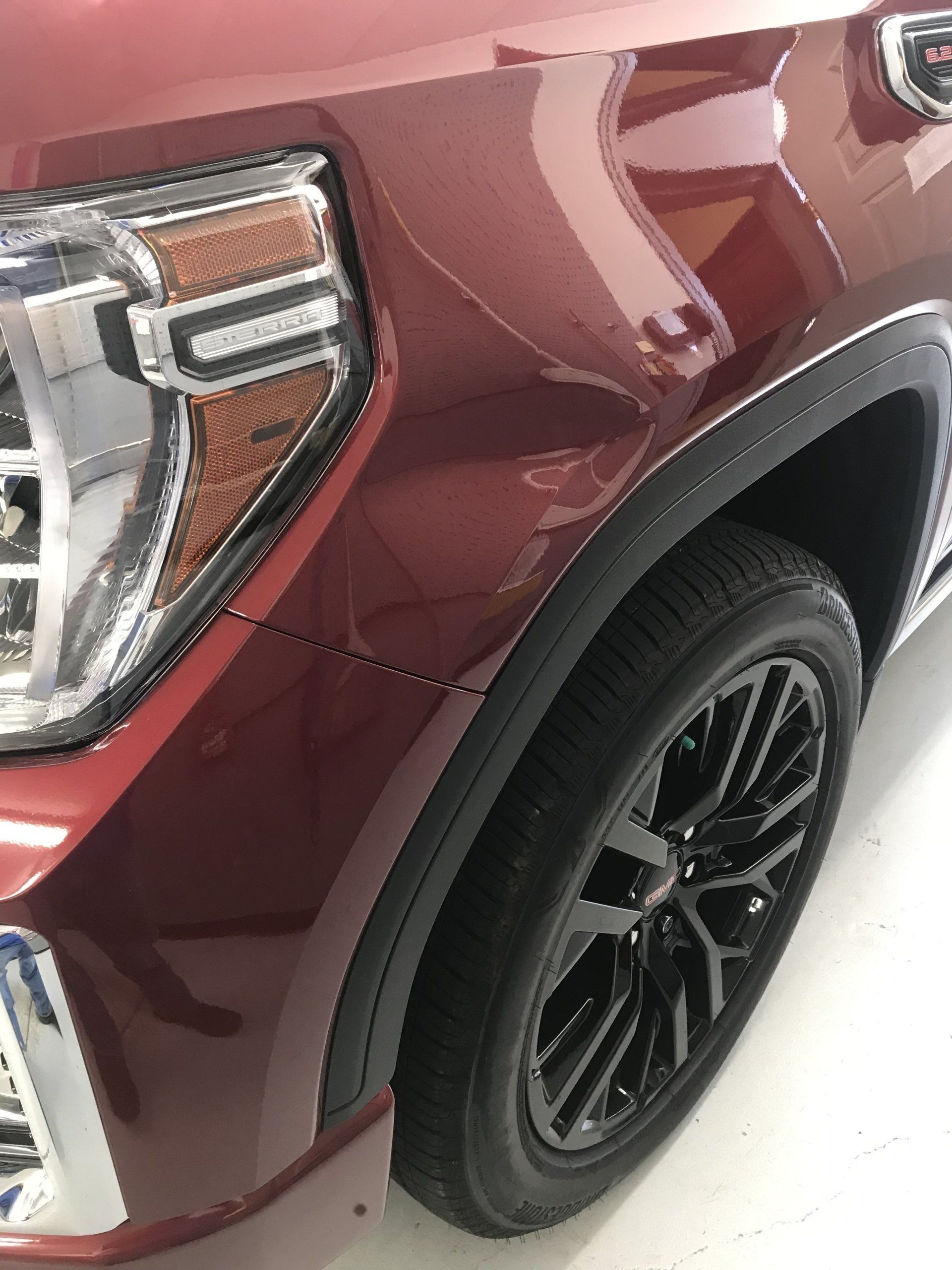 Red GMC Sierra truck front quarter panel with black tire and rim.