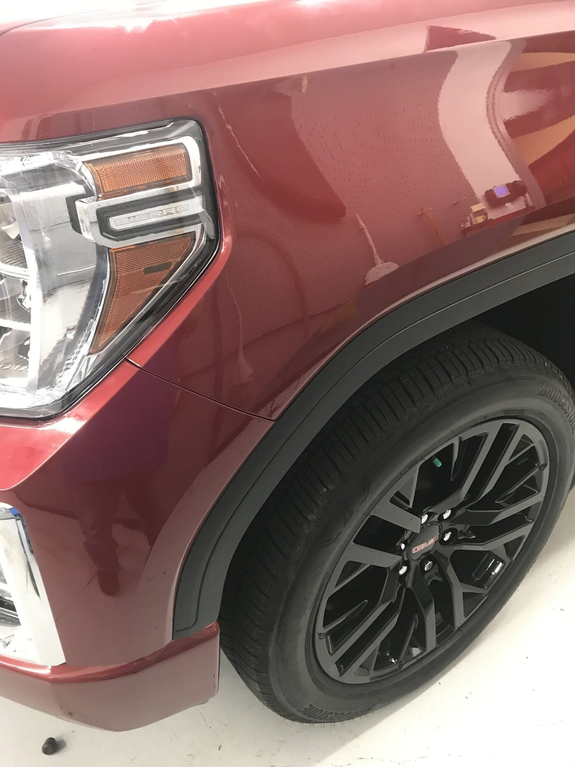 Red GMC truck front with a black wheel and headlight.