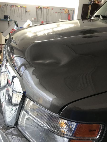 Gray car hood with a large dent; in a repair shop setting.
