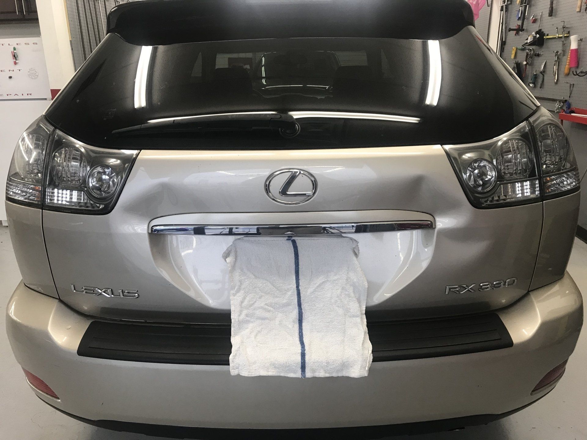 Gold Lexus SUV with a dented rear. Paper towel is stuck on the license plate area.