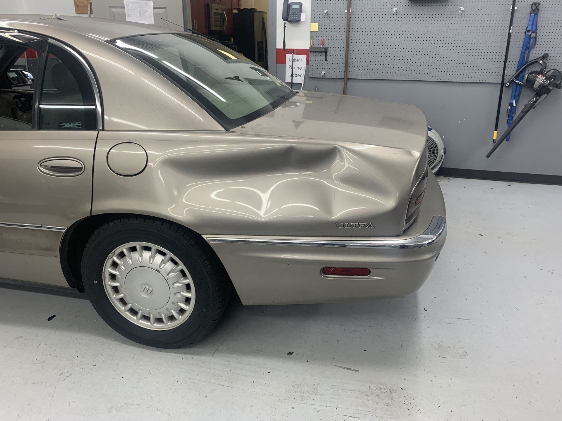 Gold sedan with significant dent in rear quarter panel in a garage.