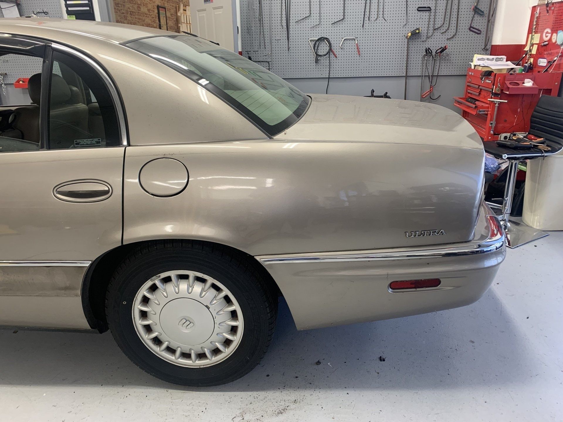 Gold Buick sedan's rear side, parked in a garage. Includes tire, taillight, and gas cap.