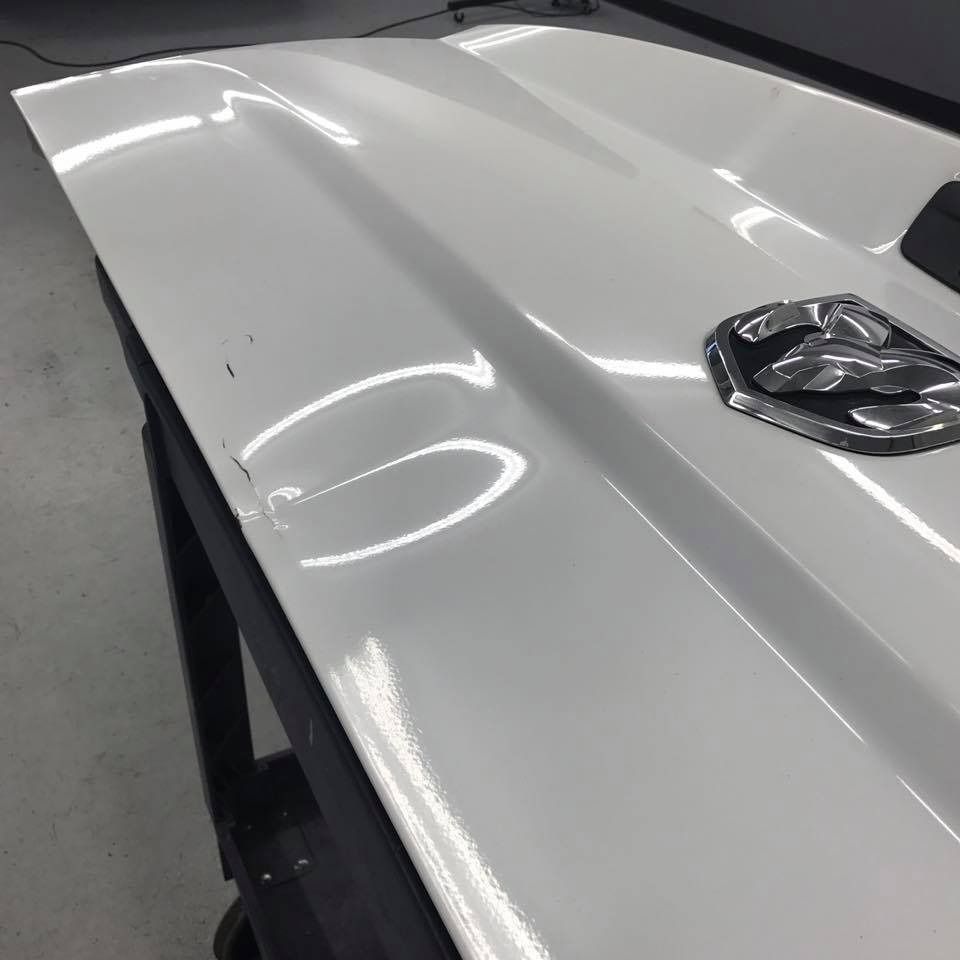 White truck hood with a dent and the Ram logo.