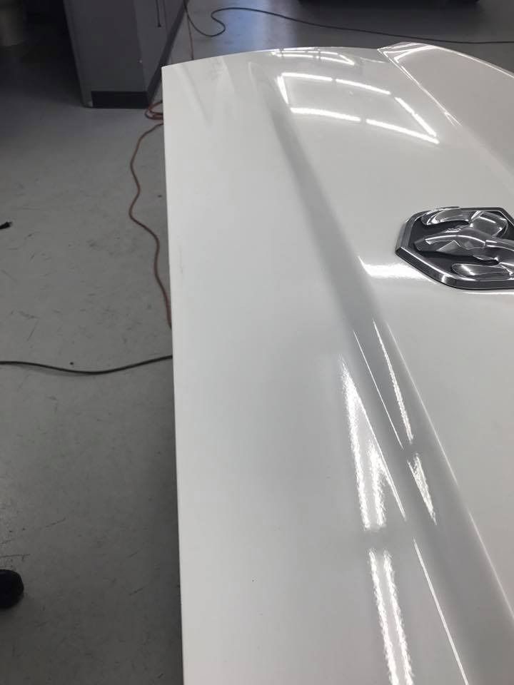 White vehicle hood with a chrome emblem in a brightly lit garage.