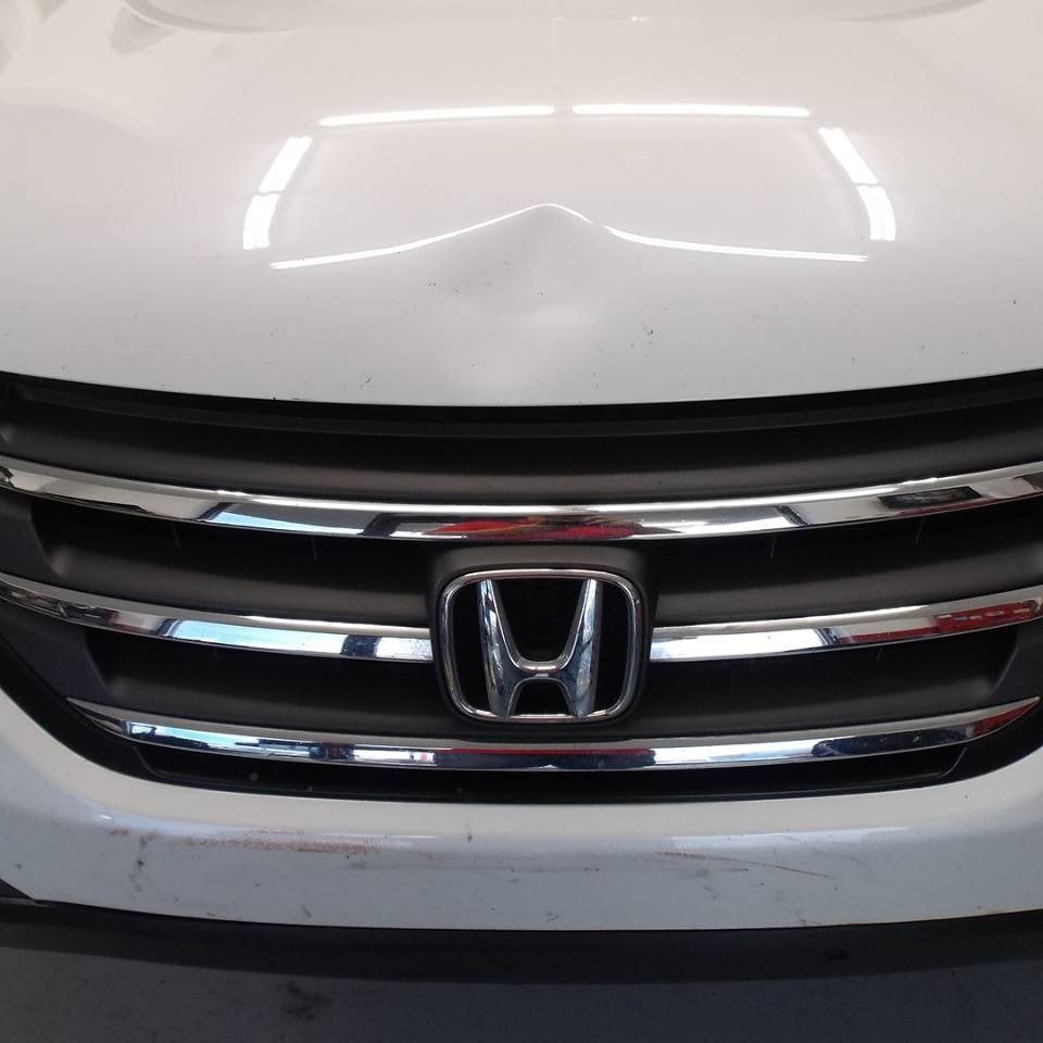 White Honda car front with chrome grill and emblem, dented hood.
