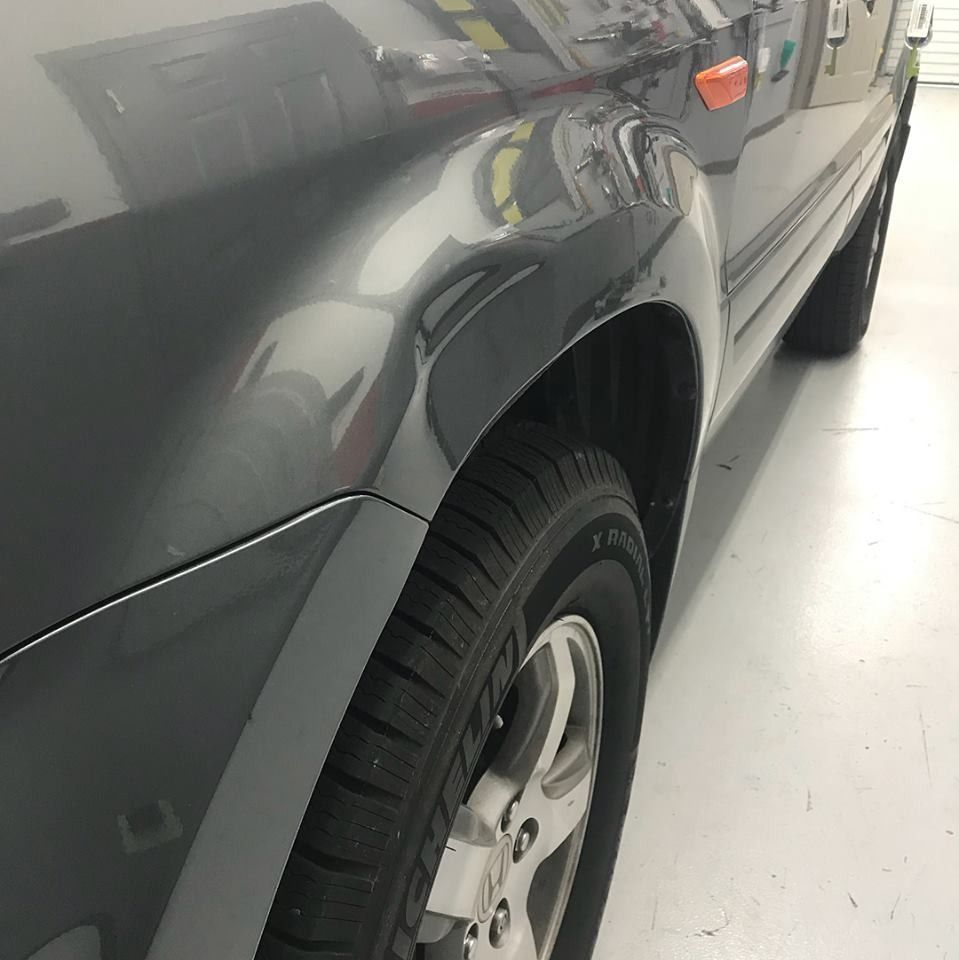 Gray car's front wheel and fender. Tires and silver rim are visible. Indoor, well-lit setting.