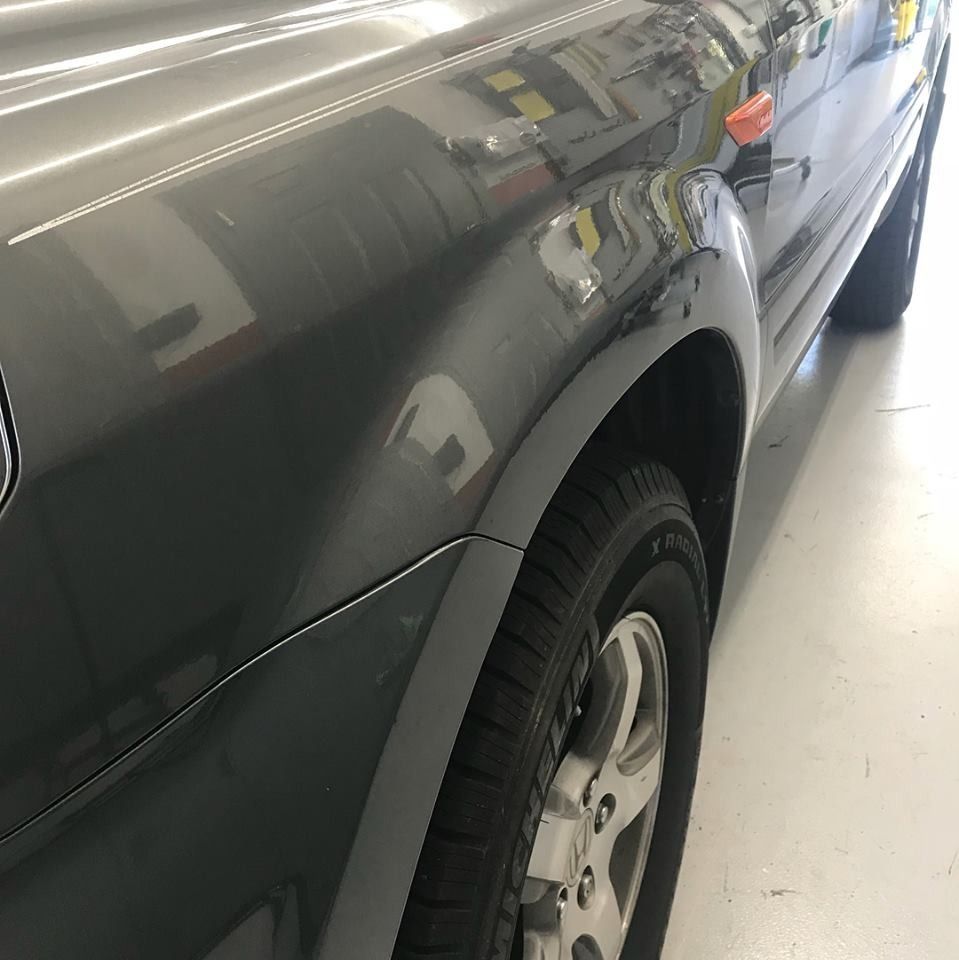 Gray car front side, fender, tire visible. Reflective surface.