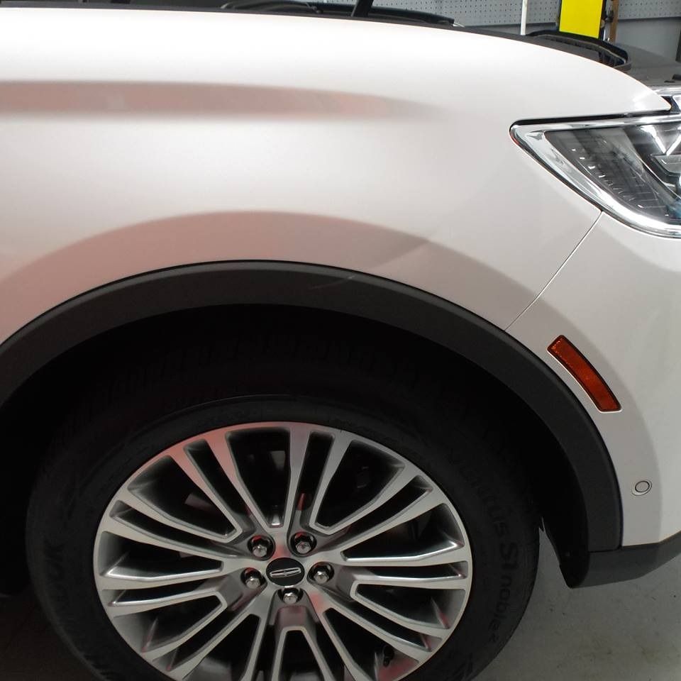 White car's front side, showing wheel, black wheel arch, and orange side marker light.