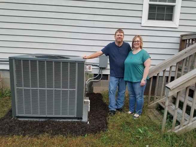 A man and a woman are standing in front of a house next to an air conditioner.