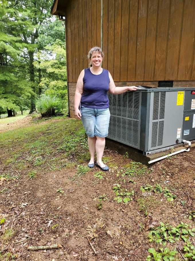 A woman is standing next to a large air conditioner.