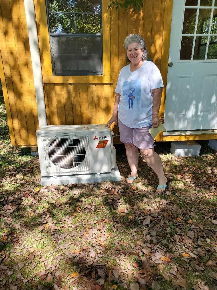 A woman is standing in front of a yellow shed holding a fan.