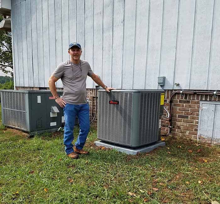 A man is standing next to two air conditioners in front of a house.