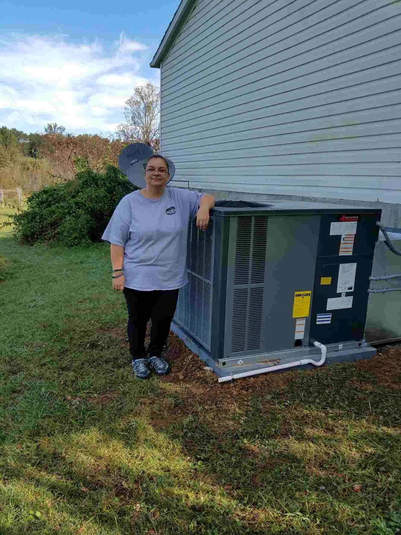 A woman is standing next to a large air conditioner outside of a house.