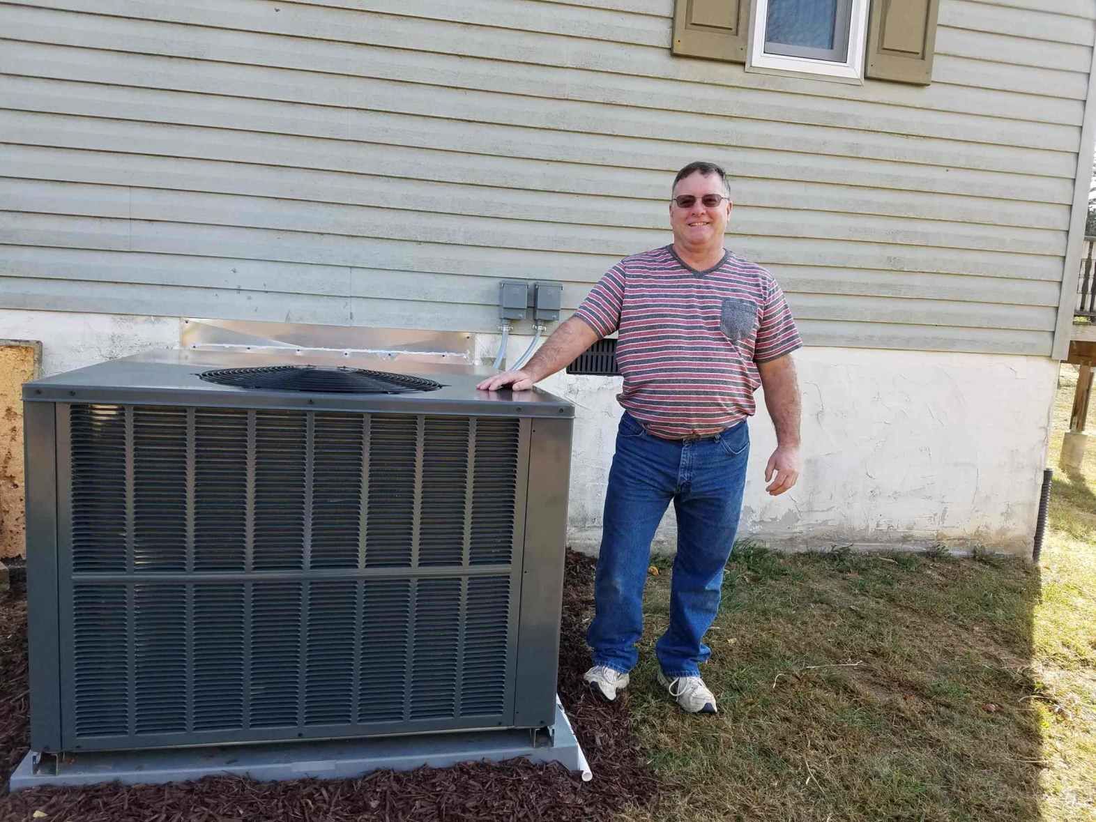 A man is standing next to a large air conditioner outside of a house.