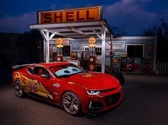 Red Lightning McQueen-style sports car parked at a Shell gas station at dusk.