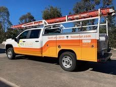 Orange utility truck with a ladder rack parked outdoors under a blue sky