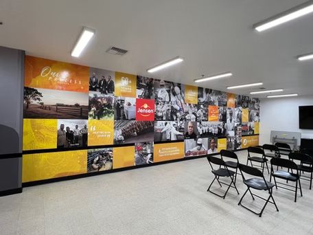 Conference room with a collage mural, folding chairs, and ceiling lights on a gray floor.