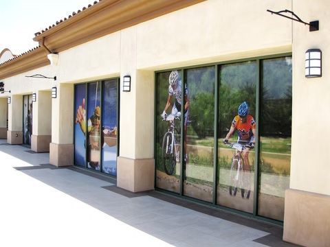 Storefront with large cyclist murals on the windows and a sunlit sidewalk outside