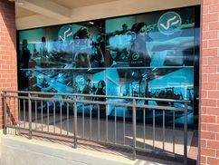 Storefront with large reflective windows, teal graphics, and a black railing in front