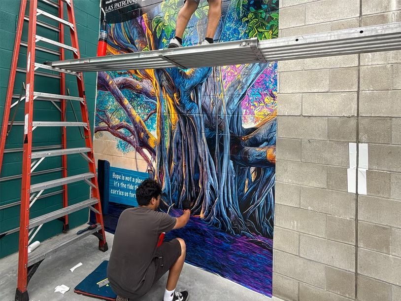 Artist painting a vibrant tree mural on a wall in a hallway with a ladder nearby